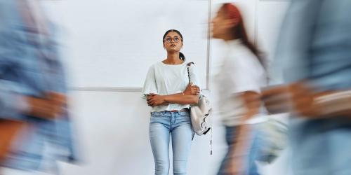 A person standing alone in a hallway with people going by 