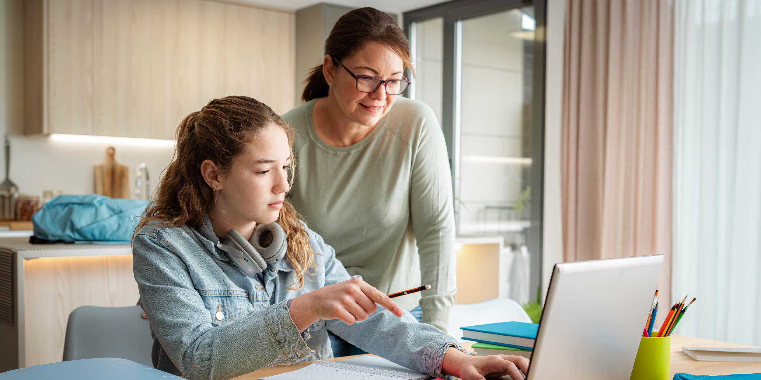 A student on her laptop and her mom standing by her and looking over