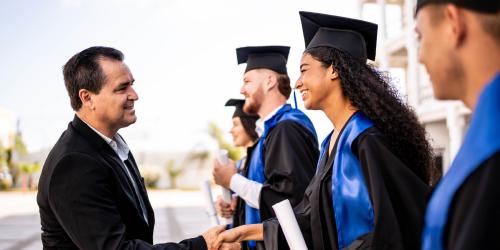 A group of graduates with one graduate shaking a person's hand