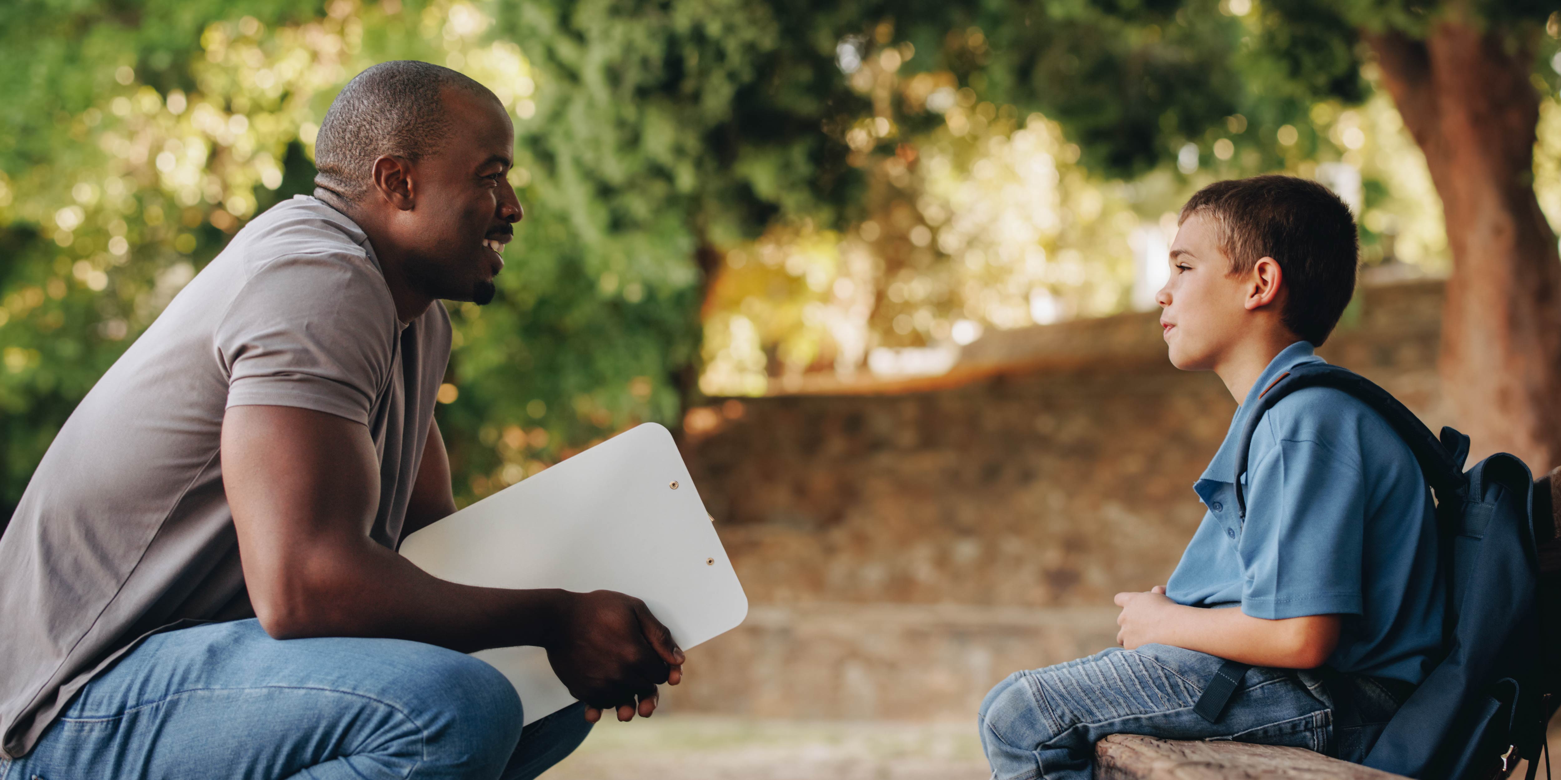A person kneeling down talking to a child with a backpack